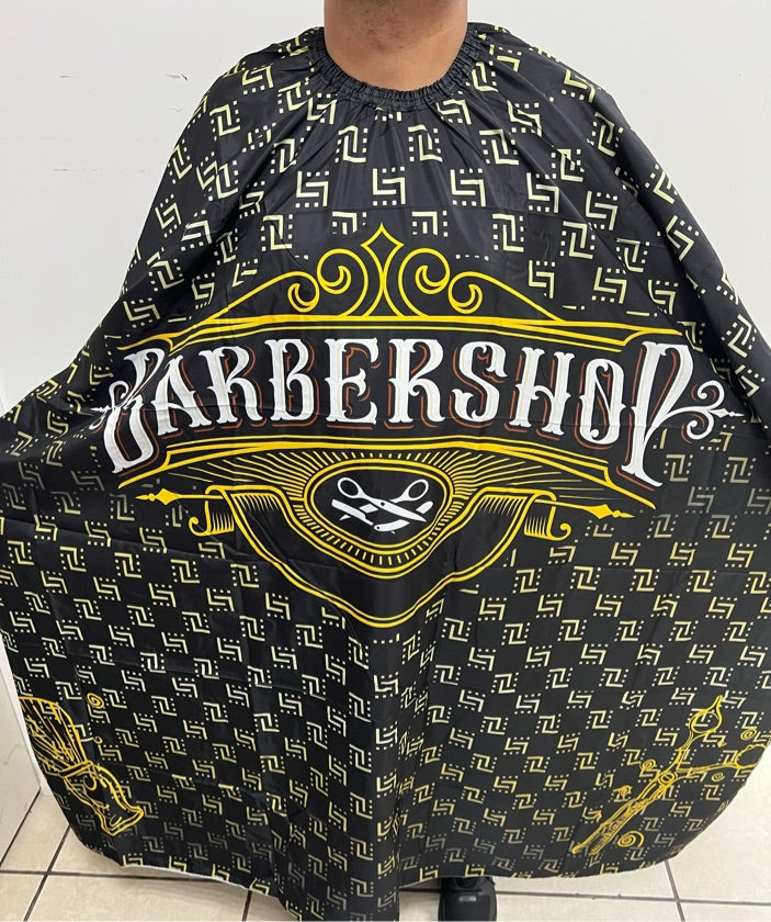 A professional salon cape with a black and yellow paisley pattern being worn by a person standing on a tiled floor.