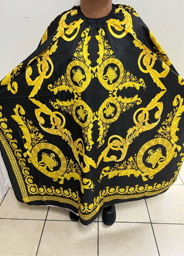 A professional salon cape with a black and yellow paisley pattern being worn by a person standing on a tiled floor.