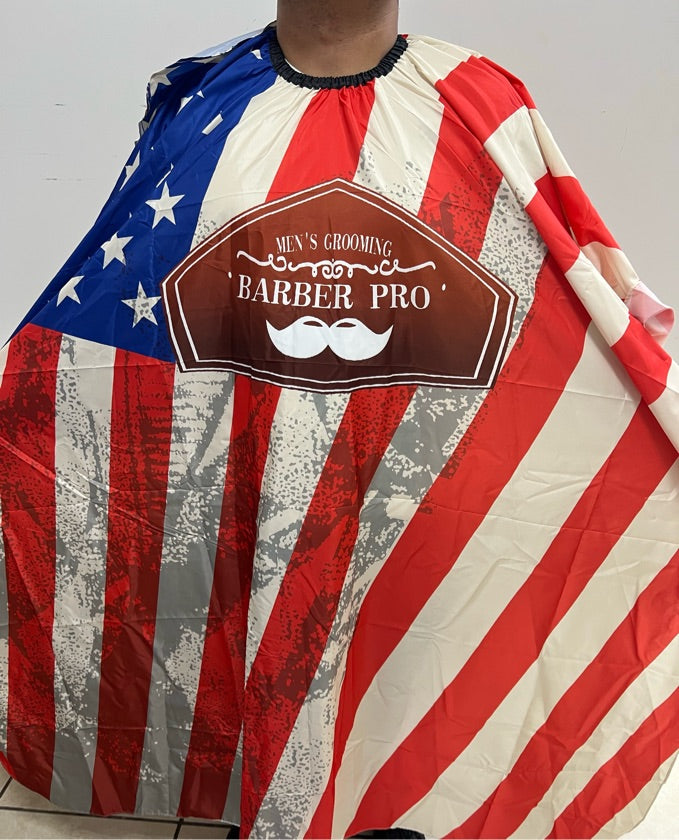A professional salon cape with a print resembling the American flag, predominantly red and white with blue stars, and the 'Barber Pro' brand logo at the top.