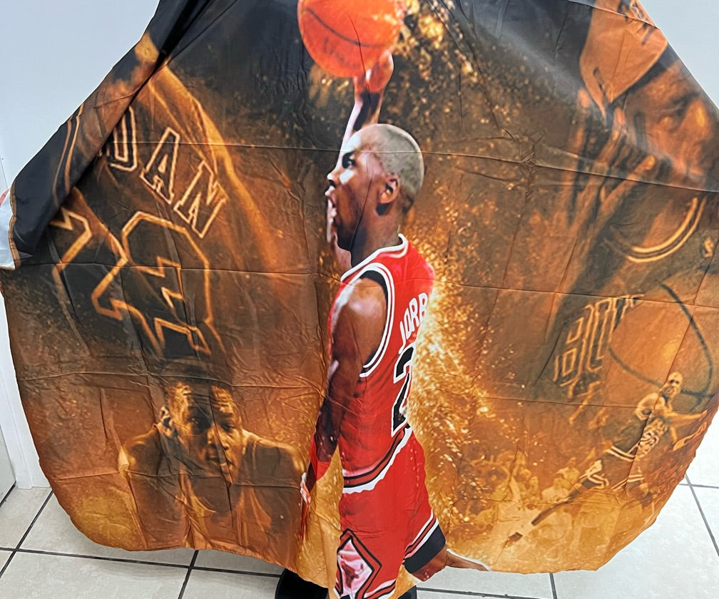 A professional salon cape with a basketball player print, predominantly featuring red, black, and yellow colors.