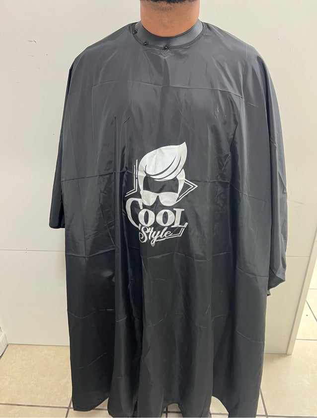 A person wearing a black cape with the text 'Cool Style' on it, presumably a barber or salon staff.