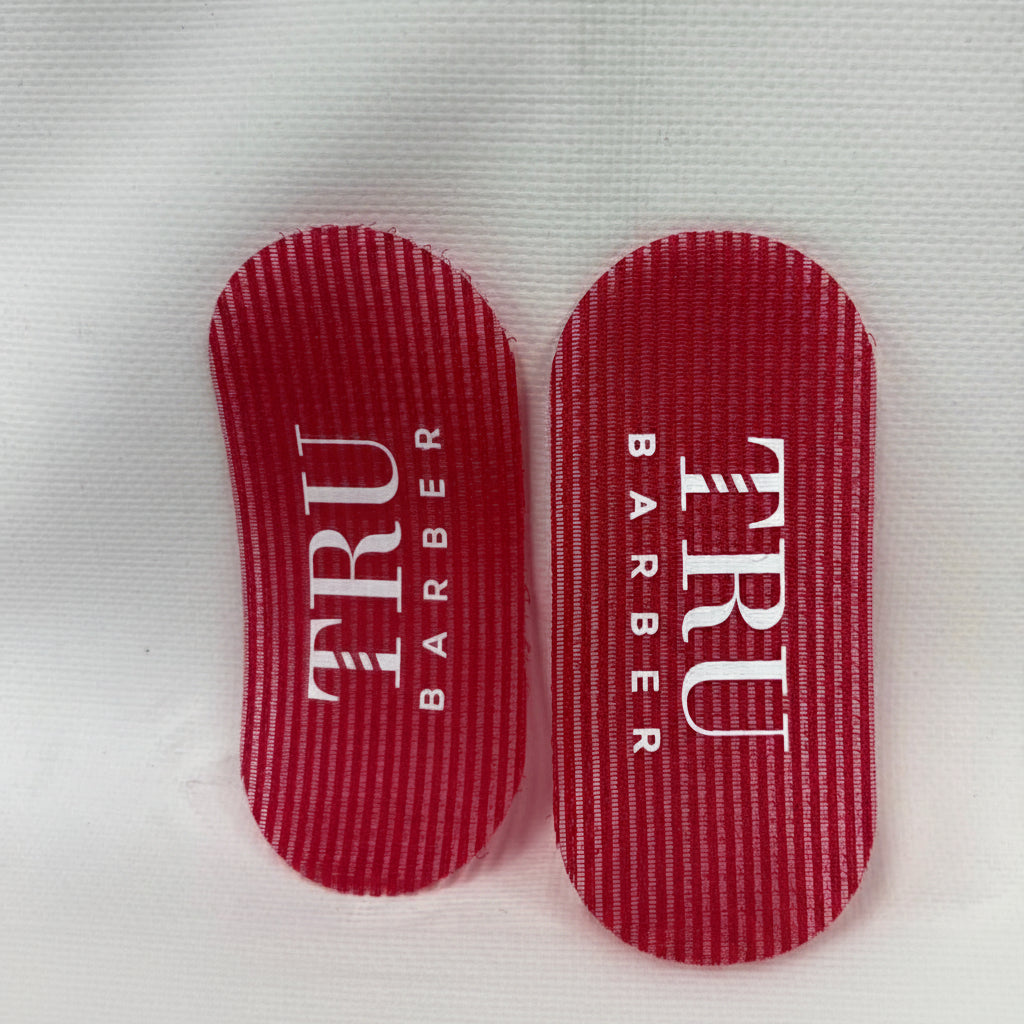 Two red hair gripers with 'TRU BARBER' text on them placed on a white background.